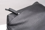 Close-up of a black genuine leather handbag with grain texture and zipper detail