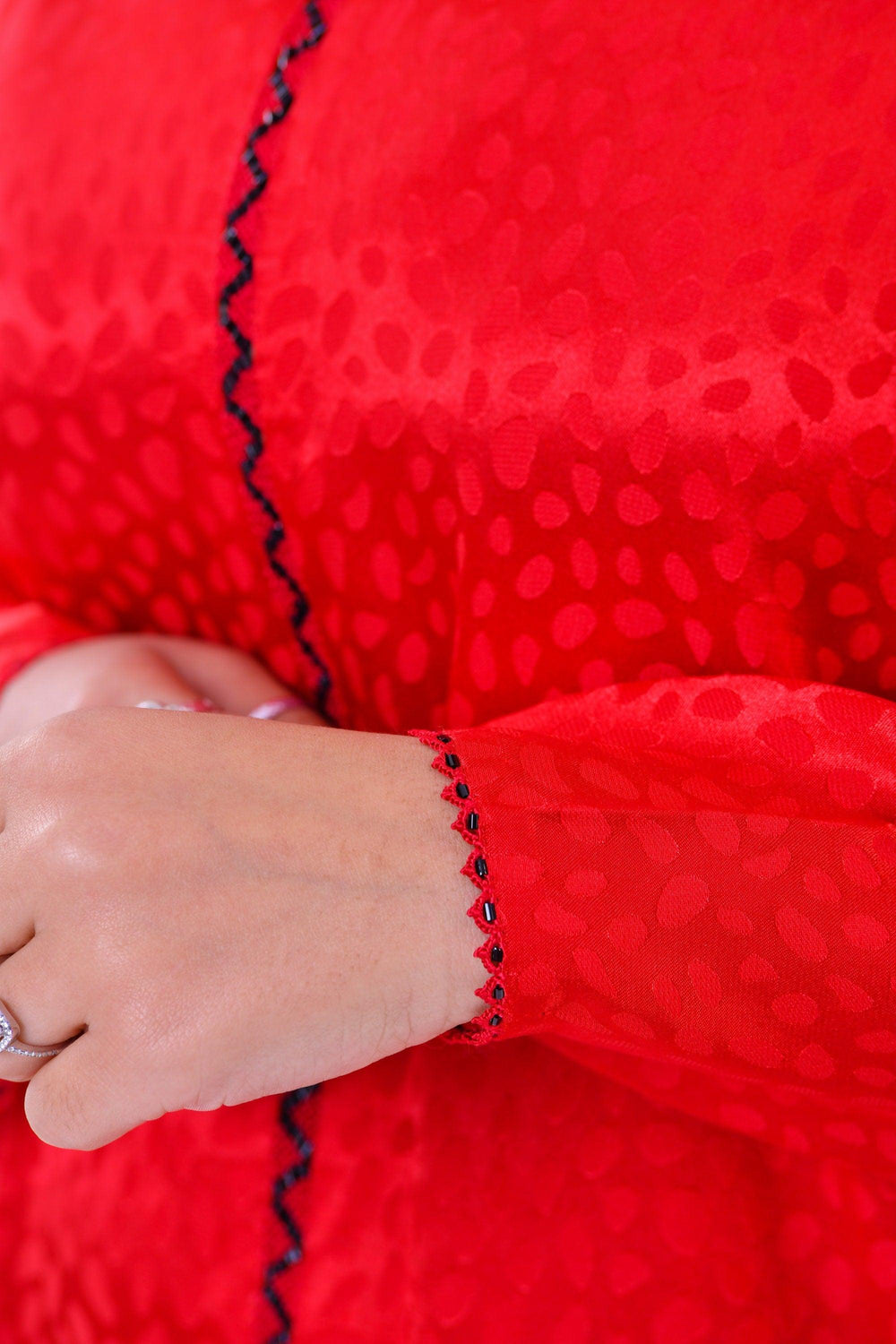 Close-up of a red silk boho dress sleeve with black embroidered trim and subtle textured pattern