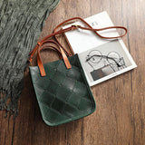 Handcrafted green cowhide leather shoulder bag with brown straps on wooden surface