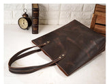 Large handcrafted dark brown leather tote bag with double handles on a white table.