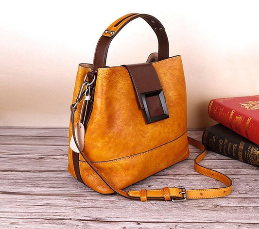 Handcrafted tan leather handbag with shoulder strap and buckle detail on wooden surface