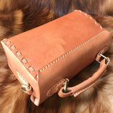 Handcrafted tan leather shoulder bag with stitched details on a fur surface
