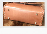 Handcrafted tan leather shoulder bag with metal feet and stitched edges on fur surface