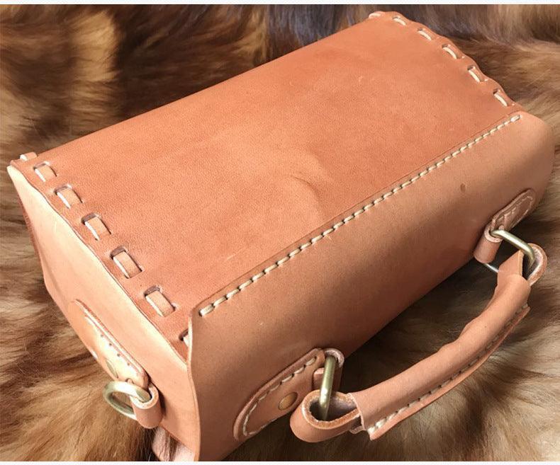 Handcrafted tan leather shoulder bag with visible stitching and brass hardware on fur surface