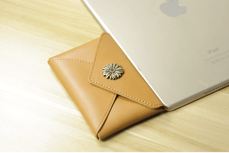 Handcrafted minimalist leather slim wallet with floral button next to silver tablet on wood surface
