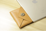 Handcrafted minimalist leather slim wallet with floral button next to silver tablet on wood surface