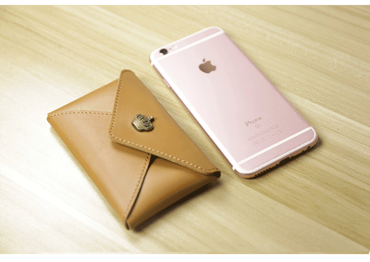 Minimalist tan leather slim wallet with clasp next to a rose gold smartphone on a wooden surface