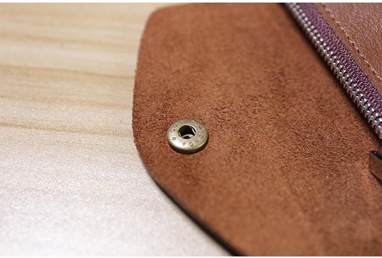 Close-up of brown handcrafted leather wallet with snap button and zipper on wood surface
