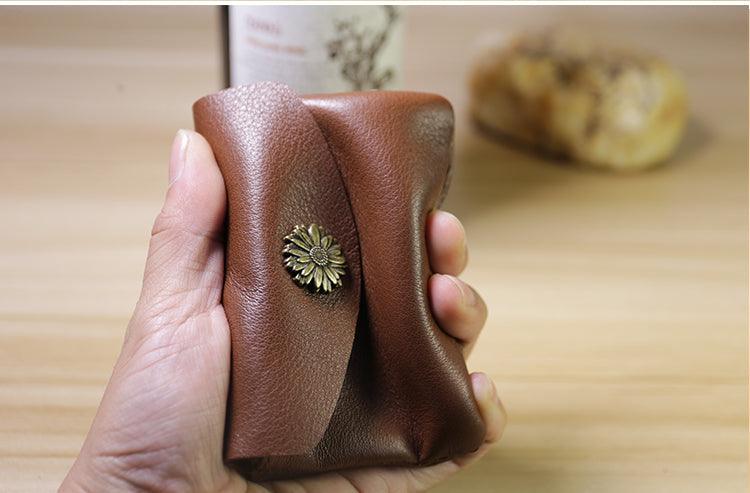 Hand holding a minimalist brown leather slim wallet with floral metal button clasp