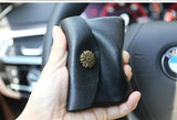 Hand holding a black handcrafted leather slim wallet with floral metal button, in car interior
