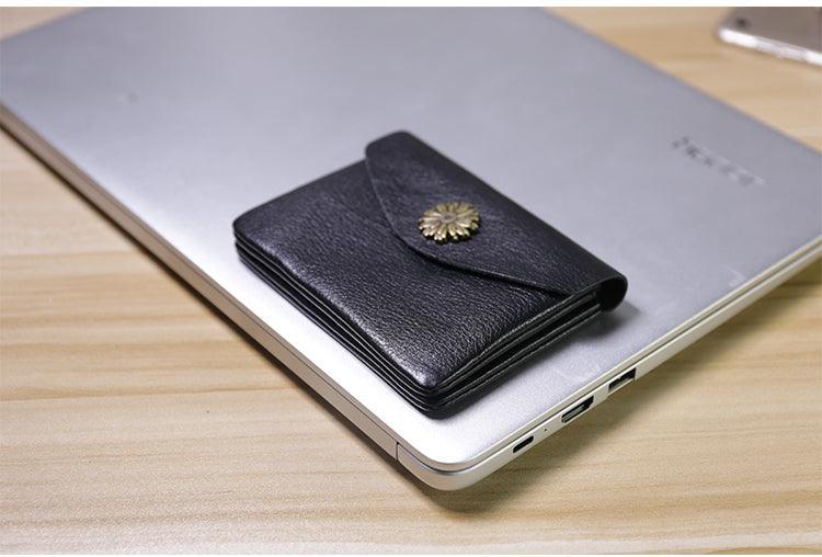 Black minimalist leather slim wallet with gold clasp on a closed laptop, modern desk setting