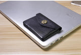 Black minimalist leather slim wallet with gold clasp on a closed laptop, modern desk setting