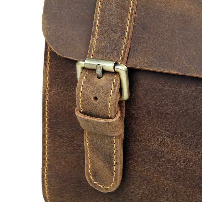 Close-up of vintage-style brown leather messenger bag with brass buckle and stitching.