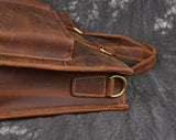 Handmade full grain leather messenger bag with brass hardware and adjustable strap on fabric background