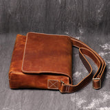 Handmade vintage cowhide leather shoulder bag with flap and adjustable strap on grey background