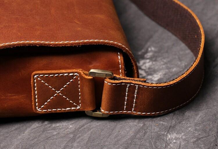 Close-up of brown cowhide leather shoulder bag with white stitching and brass hardware
