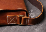 Close-up of brown cowhide leather shoulder bag with white stitching and brass hardware