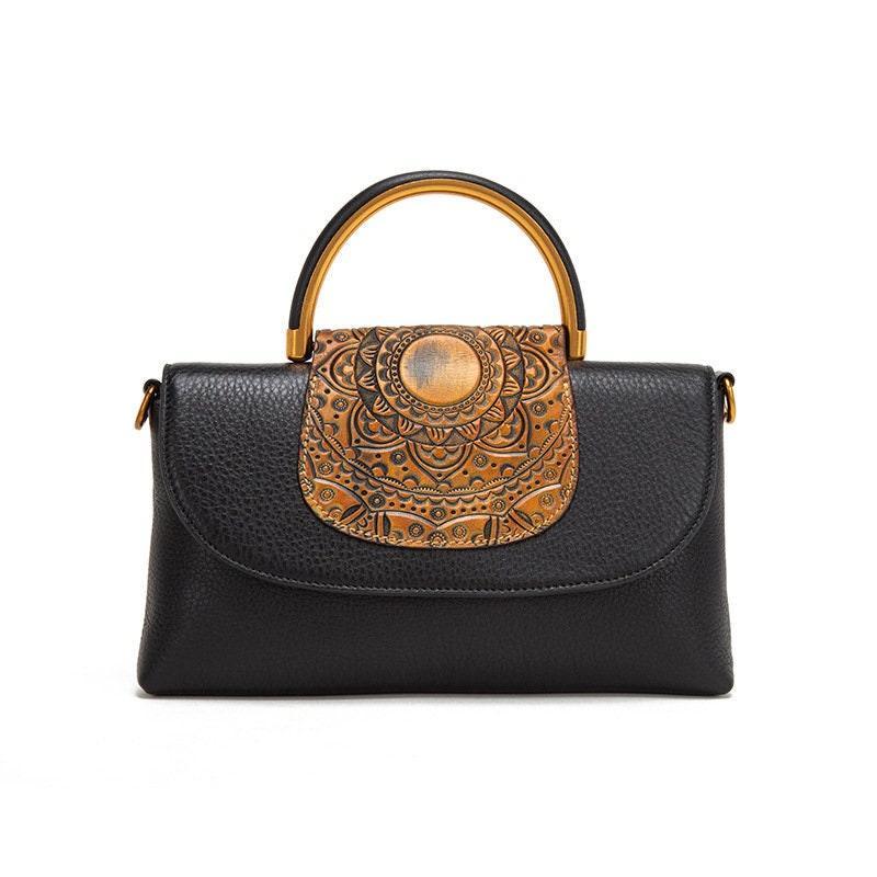 Black leather handbag with carved tan flap, mandala pattern, and gold top handle