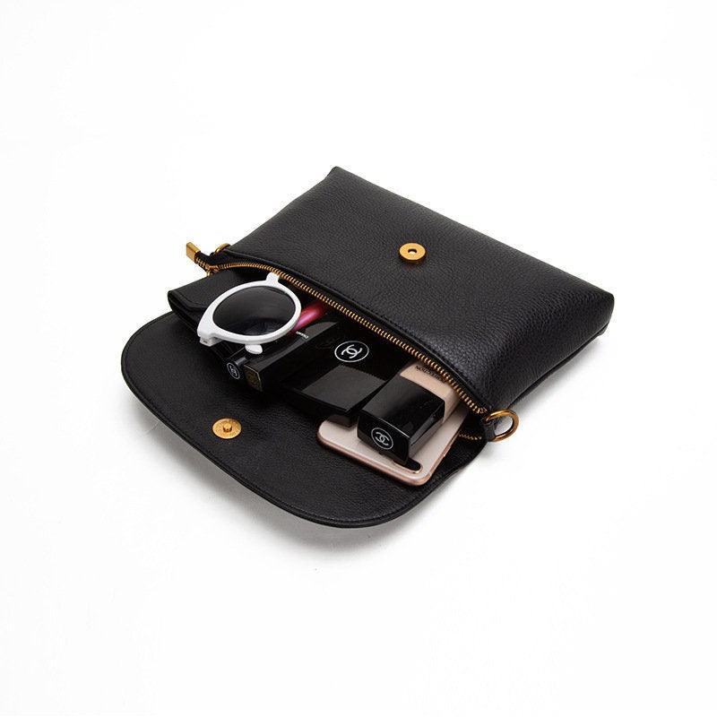 Black leather clutch bag open, displaying organized makeup, watch, and phone inside.