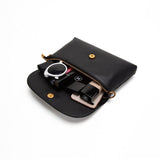 Black leather clutch bag open, displaying organized makeup, watch, and phone inside.