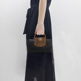Woman in black dress holding black leather handbag with embossed brown flap and top handle