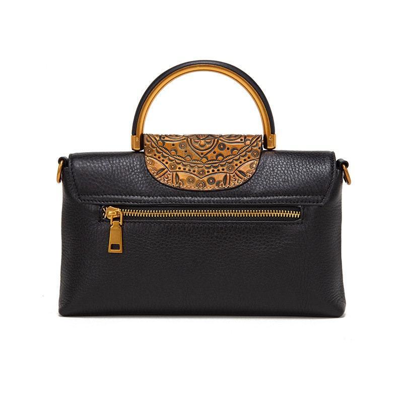Black leather handbag with gold zipper and ornate carved wooden handle on white background