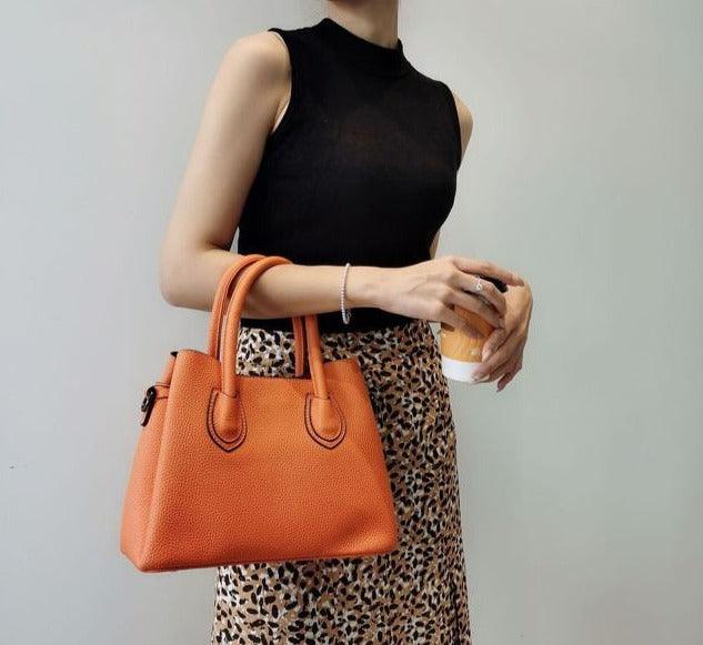Woman holding an orange leather handbag, wearing a sleeveless black top and leopard skirt