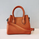 Orange leather handbag with top handles and crossbody strap on white background