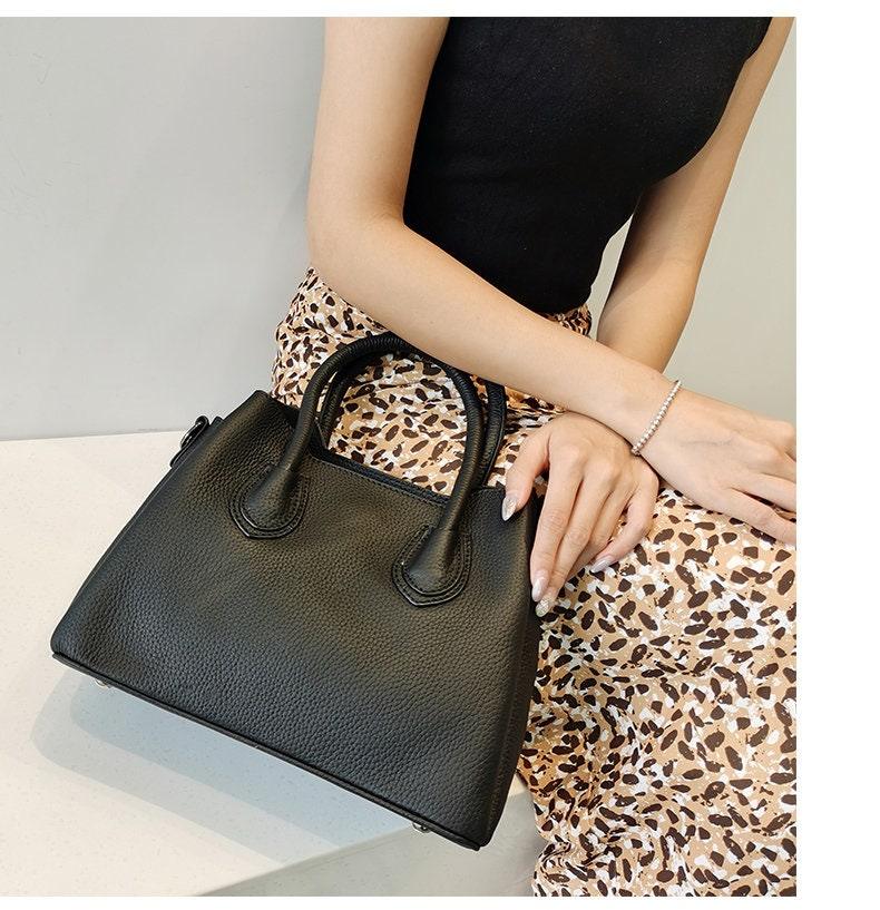 Woman holding black leather handbag with top handles, wearing animal print skirt