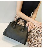 Woman holding black leather handbag with top handles, wearing animal print skirt