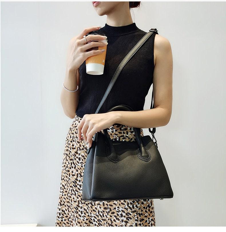 Woman holding coffee and wearing a sleeveless top, leopard skirt, and black leather handbag.