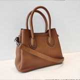 Brown leather handbag with textured finish, top handles, and shoulder strap on white surface