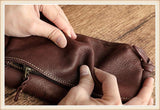 Hands squeezing a small brown cowhide leather shoulder bag on a wooden surface