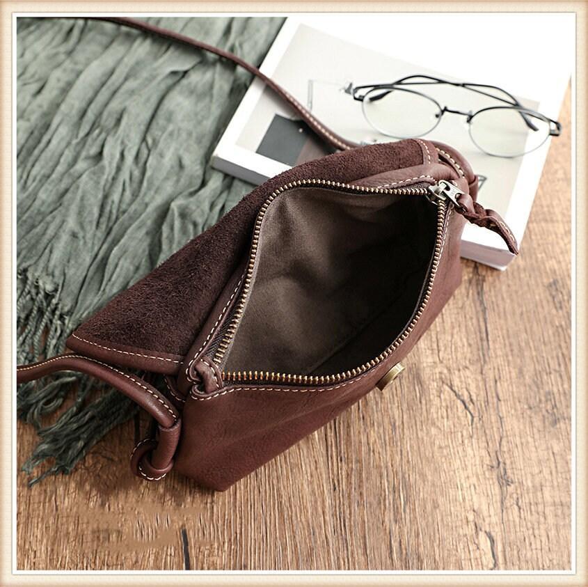 Small brown cowhide leather shoulder bag with zipper, displayed open on wooden surface