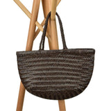 Handcrafted brown woven leather handbag with bamboo-style handles on a neutral background
