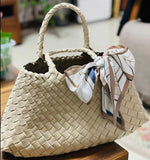 Woman holding trapezoidal woven leather hobo bag with braided handles, neutral pearl white