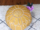 Handmade light yellow Moroccan leather pouf footstool on a textured rug, vase with pink flowers nearby