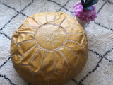 Handmade light yellow Moroccan leather pouf with decorative stitching on patterned rug, flower vase nearby