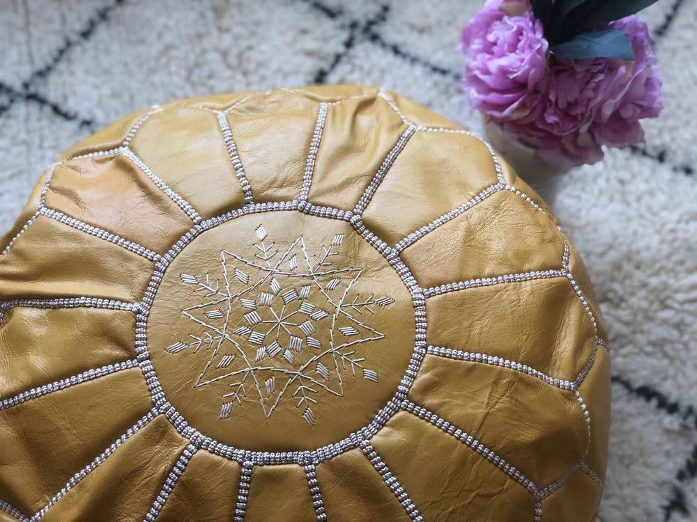Handmade light yellow Moroccan leather pouf with white patterned stitching on a textured rug