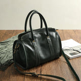 Black cowhide leather handbag with shoulder strap on wooden table, elegant and spacious design
