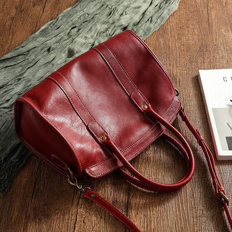 Large red cowhide leather shoulder bag with double handles and strap on wooden surface