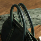 Close-up of dark green cowhide leather handbag with double handles and contrast stitching