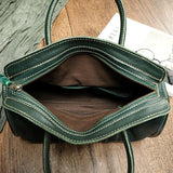 Spacious green cowhide leather handbag with zipper, brown interior, and sturdy handles on wood surface
