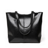 Black leather tote bag with double handles and white stitched trim on plain background