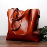 Large brown leather tote shoulder bag with double handles on wooden surface