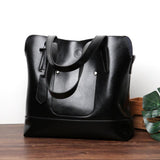 Black leather tote shoulder bag with double handles on a wooden table