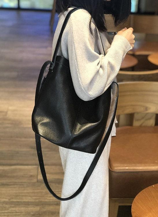 Woman wearing a large black leather bucket bag with shoulder strap in a casual indoor setting