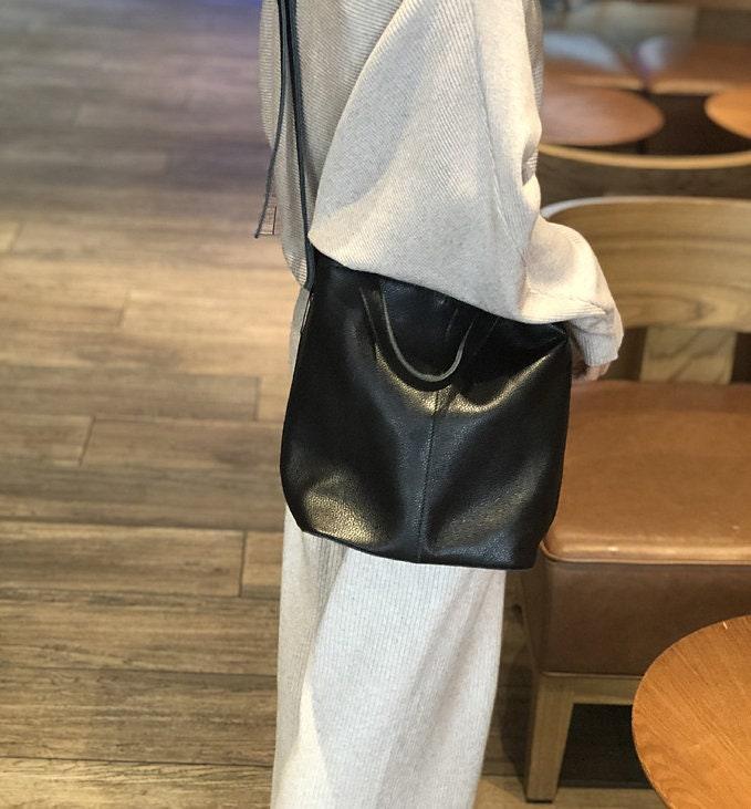 Large black leather bucket bag worn crossbody by woman in casual indoor setting