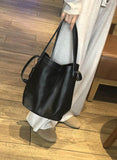 Large black leather bucket bag with shoulder strap, held by woman in neutral loungewear indoors