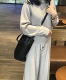 Woman wearing a grey sweater and pants with a black leather bucket shoulder bag in a cafe